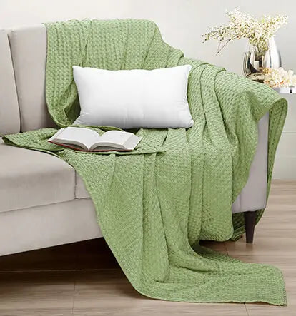 Green textured blanket draped over a beige sofa with a white pillow and open book