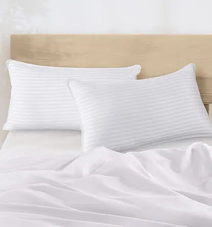White striped pillows arranged neatly on a made bed with white bedding